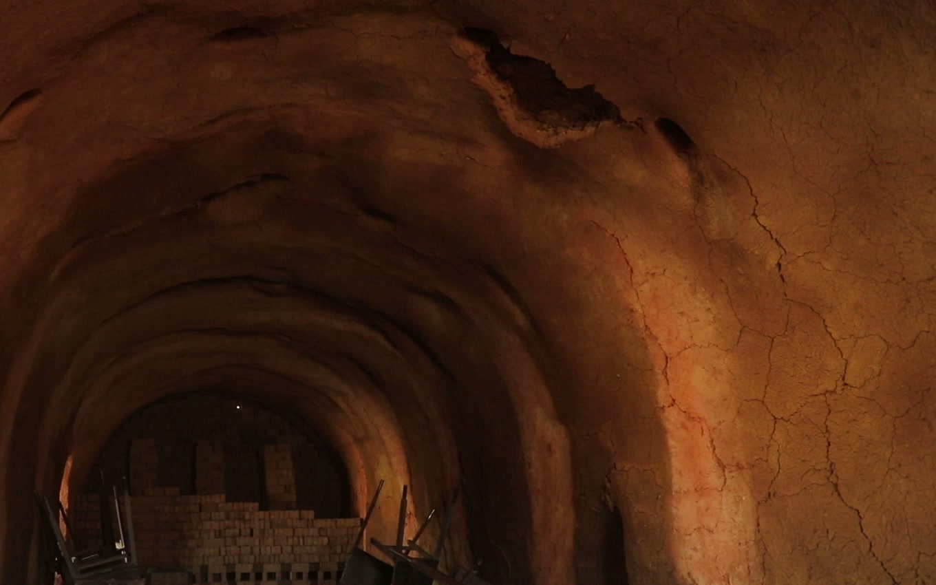 Warm light across the curved earthen walls and stacked bricks inside a kiln, from Children of the Furnace